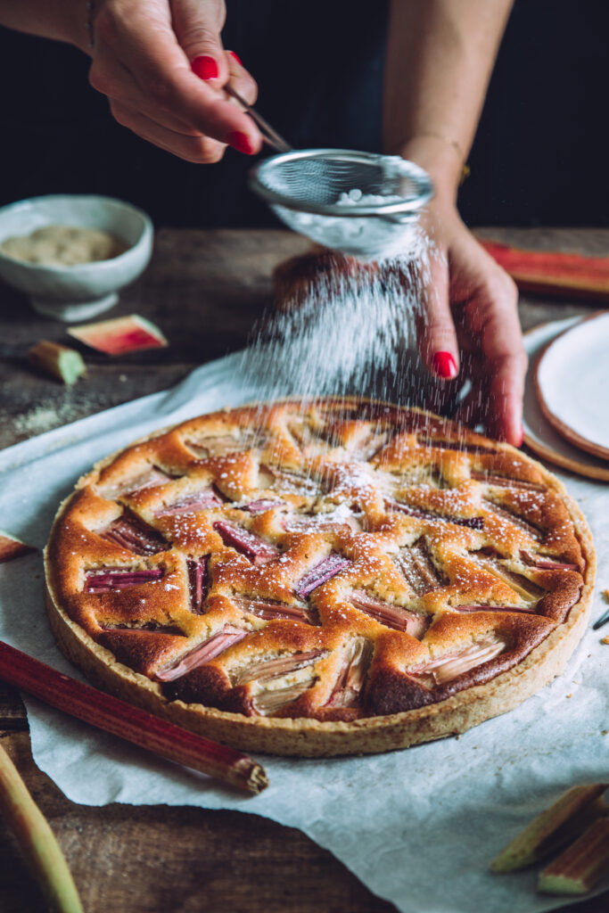 Photographie culinaire montrant une styliste culinaire en train de saupoudrer une tarte avec du sucre.
